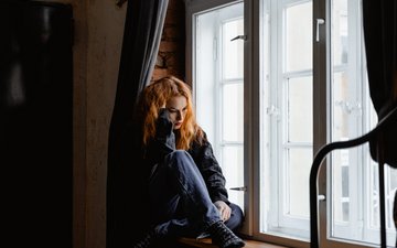 Frau sitzt grübelnd am Fenster