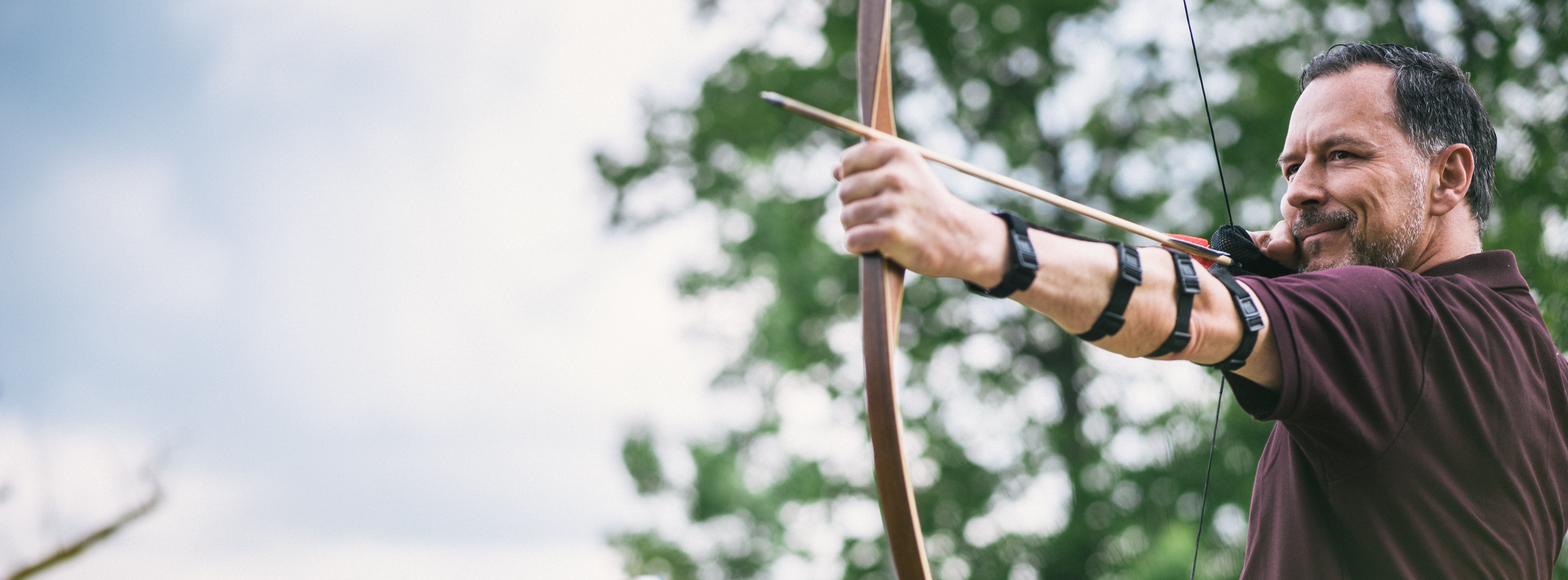 Mann mit gespanntem Pfeil und Bogen in der Hand, 2 Frauen im Hintergrund schauen zu