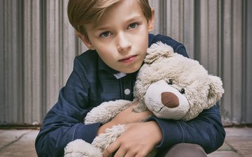 Junge mit Kuscheltier im Arm sitzt traurig da