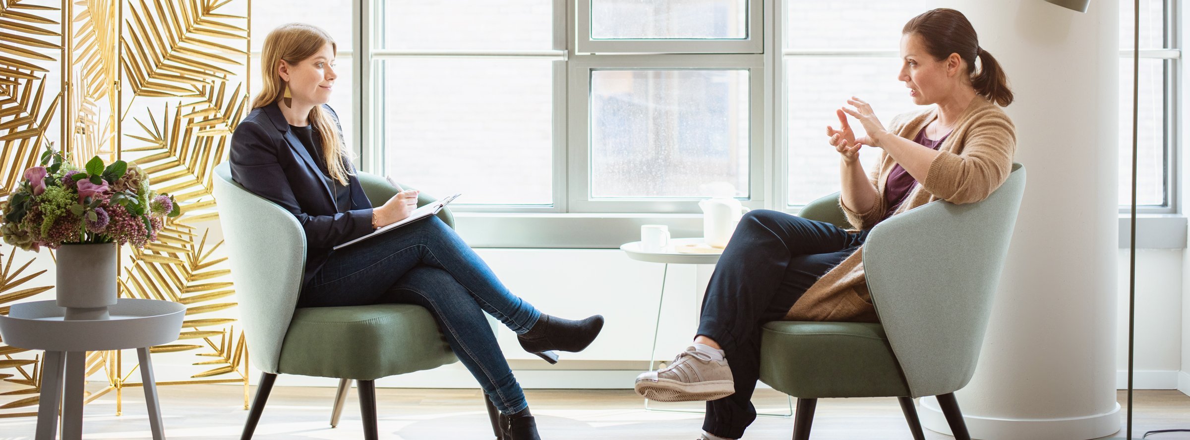 Zwei Frauen sitzen sich in hellgrünen Sesseln gegenüber und unterhalten sich