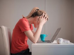 typische stresskrankheiten Frau blickt auf Laptop, schlägt Hände über dem Kopf zusammen