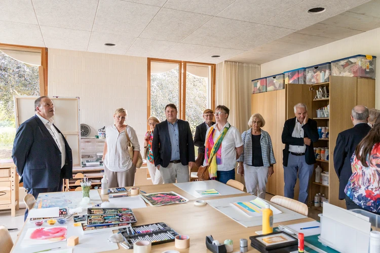 Besucherinnen und Besucher stehen in einem hellen Therapieraum mit gro&szlig;em Tisch.