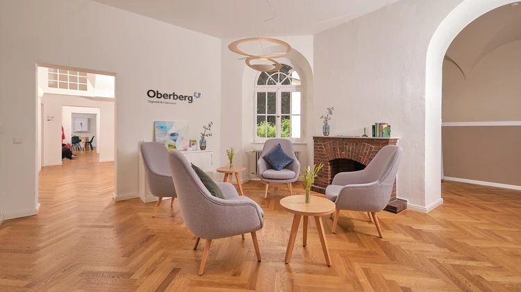 Heller Wartebereich der Oberberg Tagesklinik Hannover mit Sesseln, Kamin und Holzfu&szlig;boden