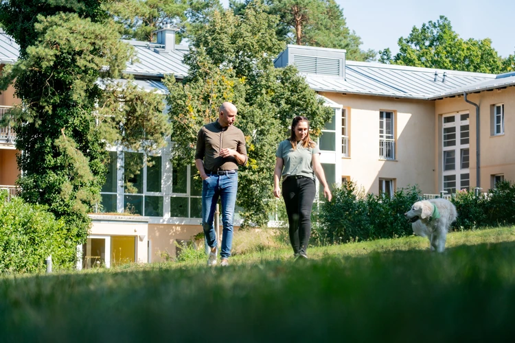 Zwei Personen spazieren mit einem wei&szlig;en Hund hinter der Oberberg Fachklinik Potsdam