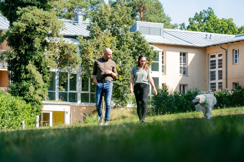 Zwei Personen spazieren mit einem wei&szlig;en Hund hinter der Oberberg Fachklinik Potsdam