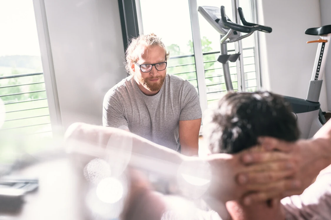 Mann mit Brille begleitet eine &Uuml;bung an einem Trainingsger&auml;t