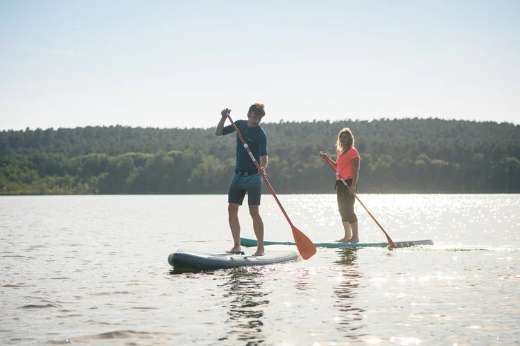 Zwei Personen stehen mit Stand-up-Paddle-Boards auf einem See