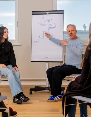 Mann erkl&auml;rt drei Personen etwas an einem Flipchart