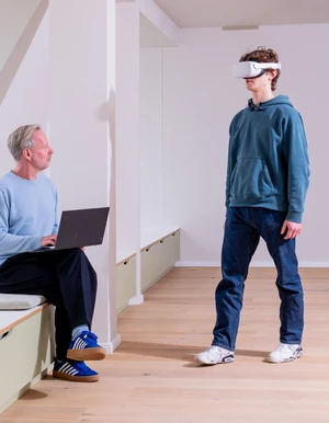 Mann mit Laptop sitzt vor Jungen mit VR-Brille