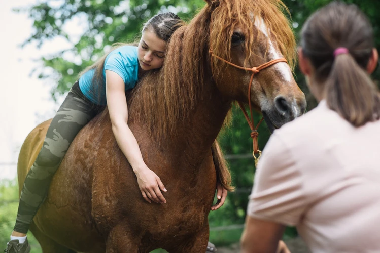 Junge Person lehnt sich auf ein Pferd, w&auml;hrend eine weitere Person danebensteht