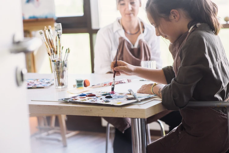 Zwei Personen arbeiten mit Malmaterialien an einem Tisch