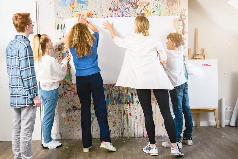 Gruppe arbeitet gemeinsam an einem Plakat an bunter Wand