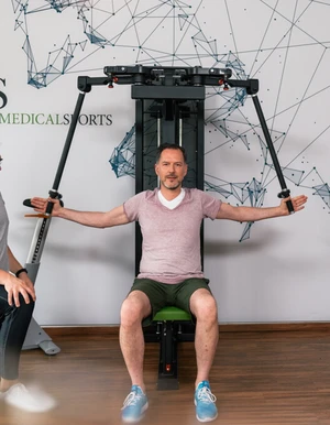 Mann begleitet eine Person bei einer &Uuml;bung im Fitnessraum