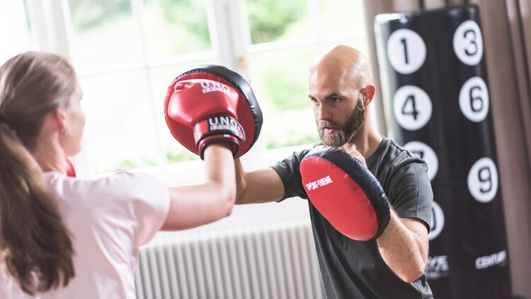 Trainer h&auml;lt einer Frau beim Boxtraining Pratzen hin