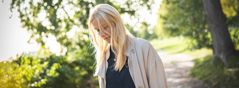 Blonde Frau geht nachdenklich auf einem sonnigen Weg im Gr&uuml;nen