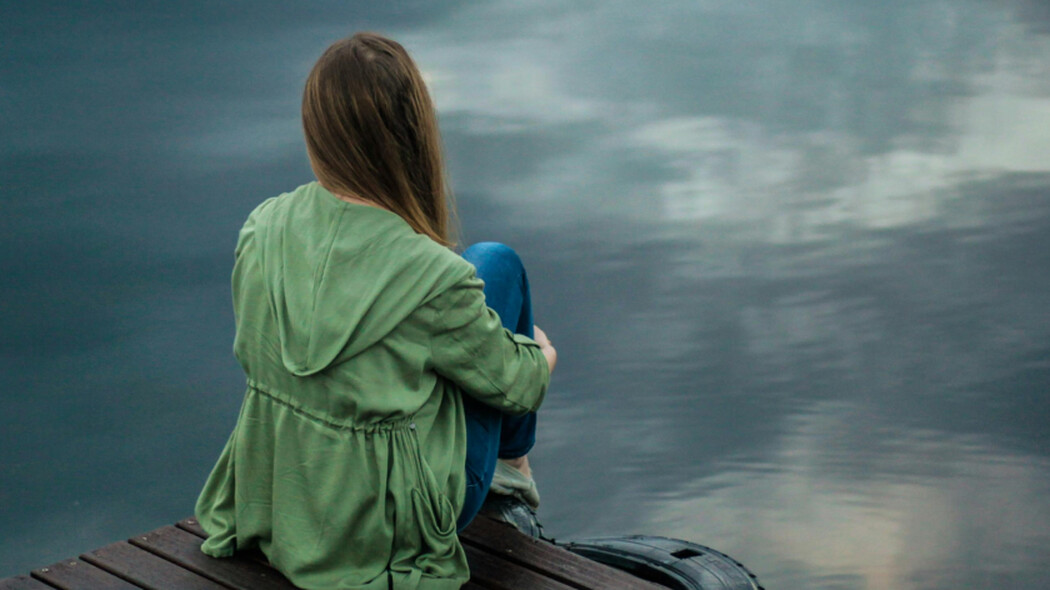 Person sitzt auf einem Steg und blickt auf ruhiges Wasser