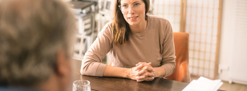 Frau sitzt in einem hellen Raum an einem Tisch im Gespr&auml;ch