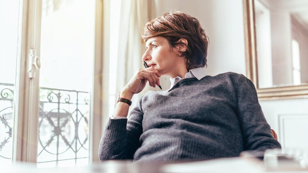 Frau sitzt nachdenklich am Fenster in einem hellen Raum