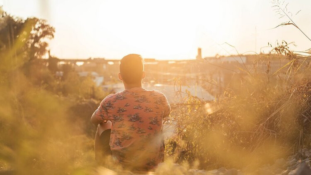 Mann sitzt bei Sonnenuntergang im Freien und blickt auf die Stadt