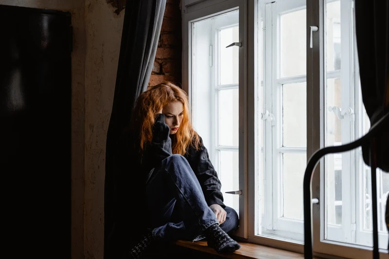 Junge Frau sitz vor dem Fenster und guckt ersch&ouml;pft