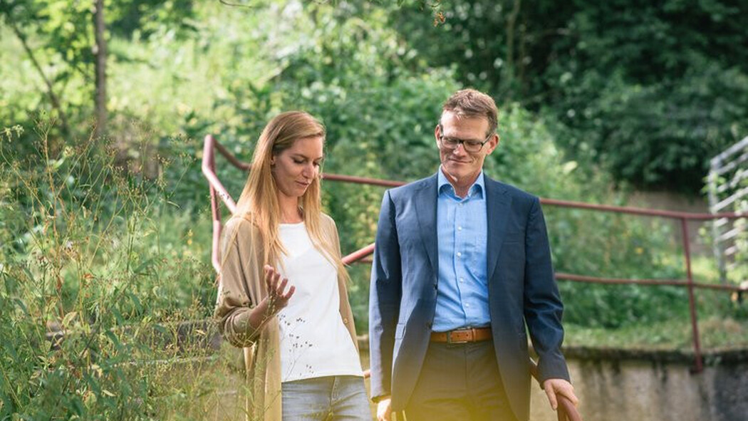 Frau und Mann gehen im Gespr&auml;ch eine Au&szlig;entreppe im Gr&uuml;nen hinunter