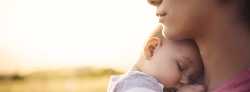 Nahaufnahme eines schlafenden Babys an der Schulter einer erwachsenen Person