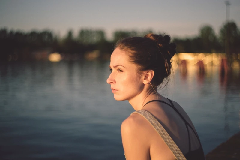 Frau sitzt am wasser ufer und schaut zur sonne